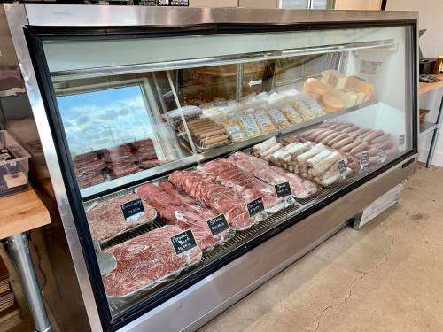 A display case filled with various cuts of meat, sausages, and packaged products in a butcher shop.