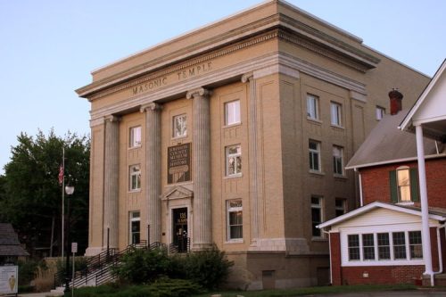 Historic Masonic Temple building with a grand facade, featuring columns and a prominent sign, surrounded by trees and houses.