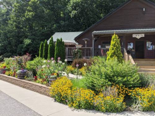 A charming wooden building with a sign reading "Open," surrounded by vibrant flower gardens and greenery.