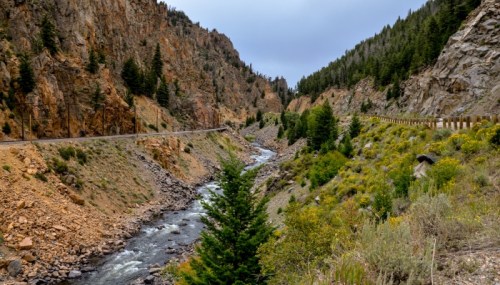 A winding river flows through a rocky canyon, flanked by steep cliffs and lush greenery under a cloudy sky.