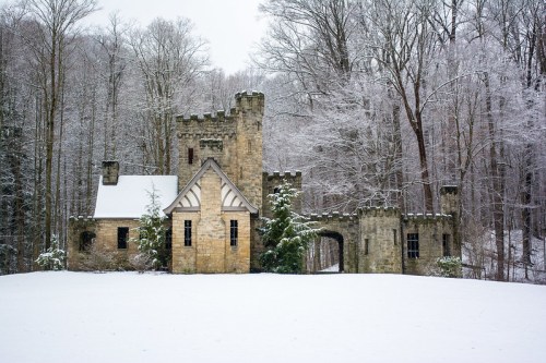 A snow-covered stone castle surrounded by trees in a winter landscape.