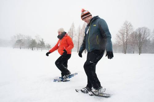 Two people snowshoeing through a snowy landscape, wearing winter clothing and enjoying a snowy day.