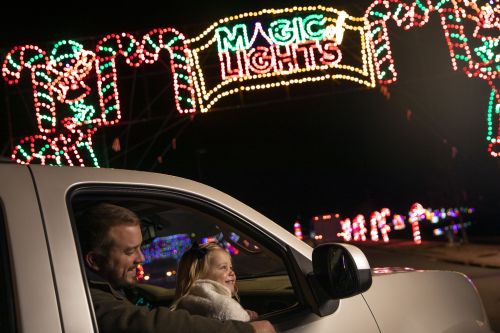 A man and a girl smile from a car, enjoying colorful holiday lights in the night. A sign reads "Magic Lights."