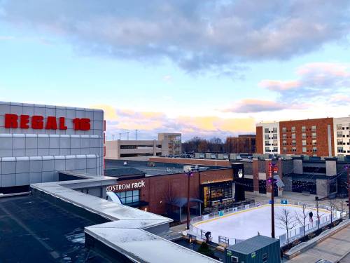 View of an outdoor ice rink surrounded by buildings, with a Regal cinema sign visible in the foreground.