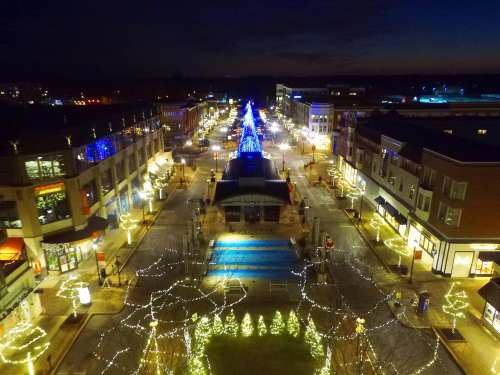 Aerial view of a festive shopping district illuminated with holiday lights and decorations at night.