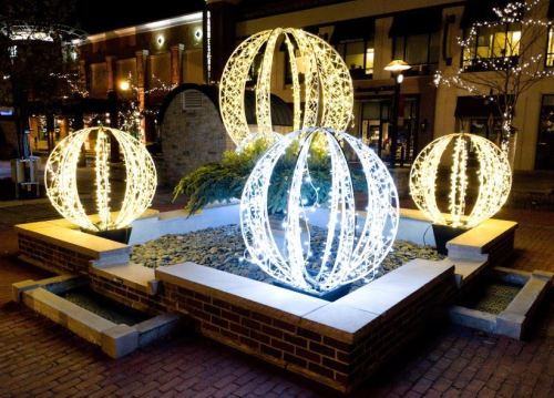 Illuminated decorative spheres in a plaza, surrounded by rocks and greenery, creating a festive nighttime atmosphere.