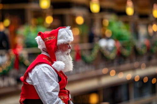 A man dressed as Santa Claus sits quietly, wearing a red outfit with white trim, surrounded by festive decorations.
