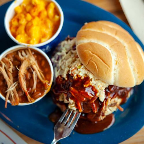 A plate featuring a pulled pork sandwich with barbecue sauce, macaroni and cheese, and baked beans on the side.
