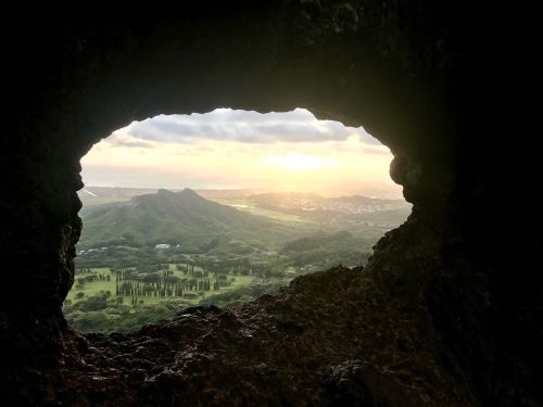 View of a lush green landscape and sunset through a rocky opening, with rolling hills in the distance.