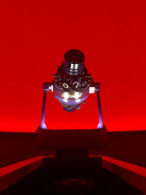 A telescope with a metallic structure, illuminated against a vibrant red background.
