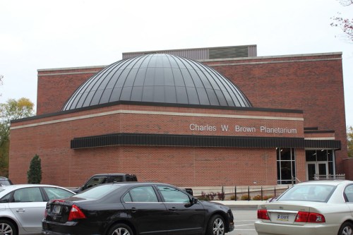 Exterior view of the Charles W. Brown Planetarium, featuring a large dome and brick facade, with parked cars in the foreground.