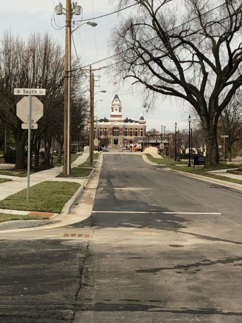 A view down a street lined with trees, leading to a historic building with a clock tower in the distance.