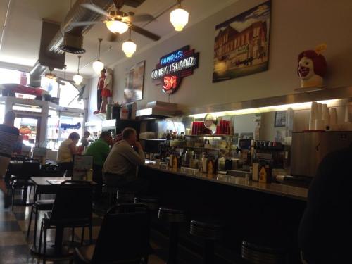 A retro diner with a long counter, patrons seated, and vintage decor including a neon sign and clown figures.