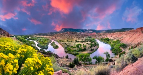 A vibrant landscape featuring a winding river, lush greenery, and colorful clouds at sunset.