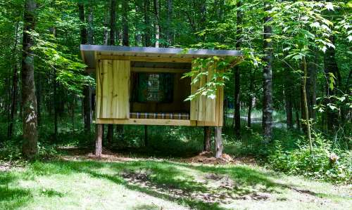 A wooden treehouse with an open front, nestled among trees in a lush green forest.