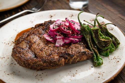 A juicy steak topped with pickled onions and served with grilled peppers on a white plate.