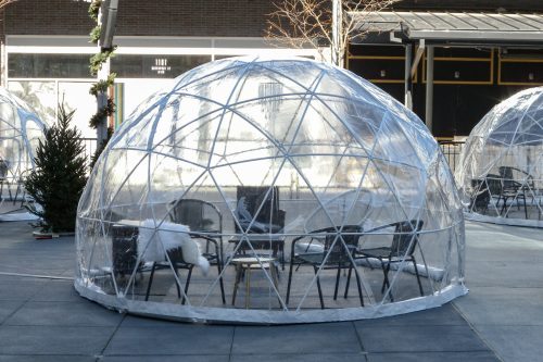 A clear plastic dome structure with chairs inside, set up outdoors in a dining area.