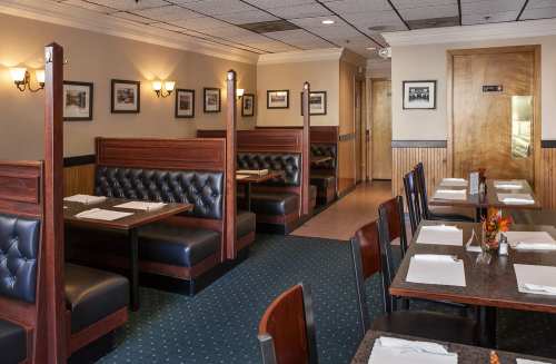 Cozy restaurant interior with dark booths, tables set with white napkins, and framed photos on the walls.