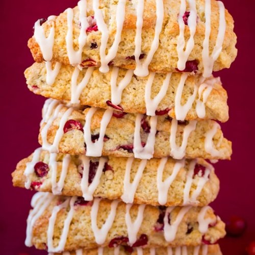 A stack of cranberry scones drizzled with white icing on a red background.