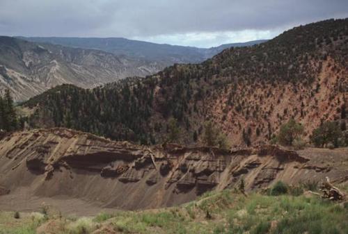 A rugged landscape featuring layered hills, trees, and a cloudy sky, showcasing geological formations and natural beauty.