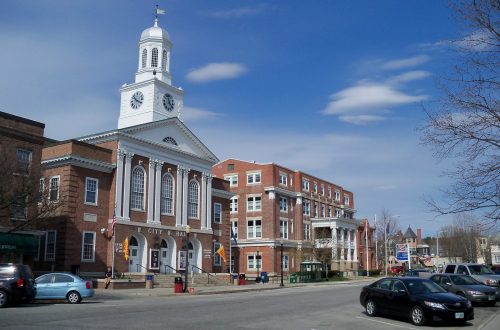 A city hall building with a clock tower, flanked by other buildings under a blue sky with scattered clouds.