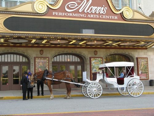 A horse-drawn carriage waits outside the Morris Performing Arts Center, with people standing nearby.