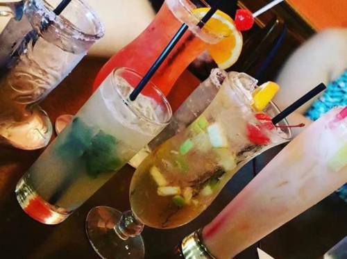 A variety of colorful cocktails with garnishes, served in tall glasses on a wooden table.