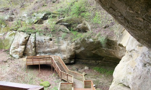 A wooden walkway leads through a rocky, green landscape with steep cliffs and vegetation.