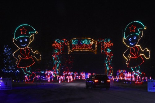 Colorful holiday lights form an archway with cheerful elf figures, welcoming visitors to a festive display.