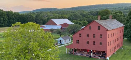 A red barn and farmhouse surrounded by lush greenery and rolling hills under a sunset sky.