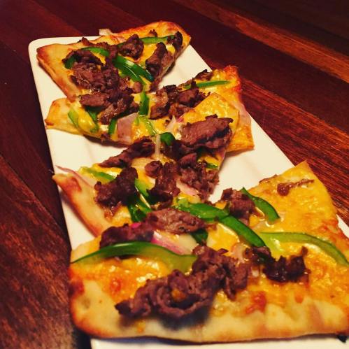 A platter of flatbread pizza topped with beef, green peppers, and onions, served on a wooden table.