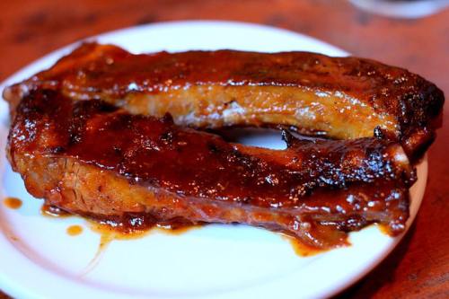 Two pieces of glazed, barbecued ribs on a white plate, glistening with sauce.