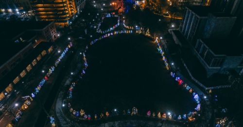 Aerial view of a park decorated with colorful Christmas lights and trees, creating a festive atmosphere at night.