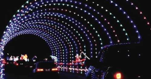 A colorful light tunnel with vibrant holiday decorations, viewed from a car at night.