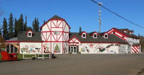 A festive building with red and white trim, decorated with holiday murals, surrounded by trees and a clear blue sky.