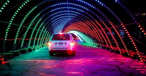 A car drives through a colorful, illuminated tunnel of red and green lights at night.