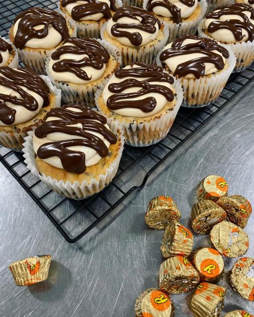 A tray of cupcakes with chocolate drizzle on top, next to scattered Reese's Peanut Butter Cups.