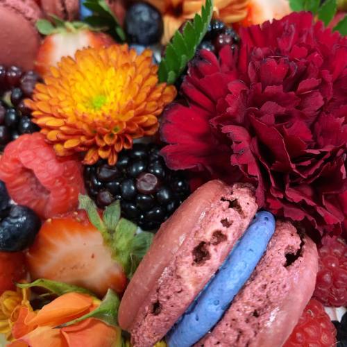 A colorful arrangement of flowers and fresh berries, featuring vibrant macarons in red and blue.