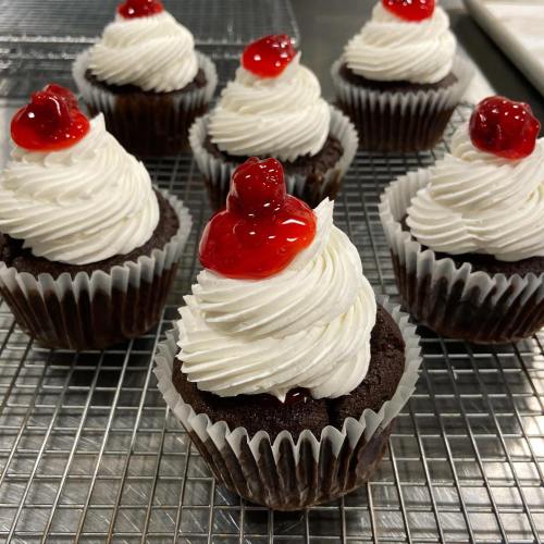 A tray of chocolate cupcakes topped with swirls of white frosting and a cherry on each.