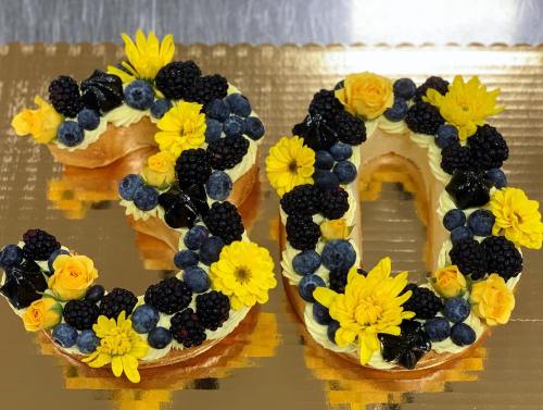 A decorative cake shaped like the numbers 3 and 0, adorned with blueberries, blackberries, and yellow flowers.