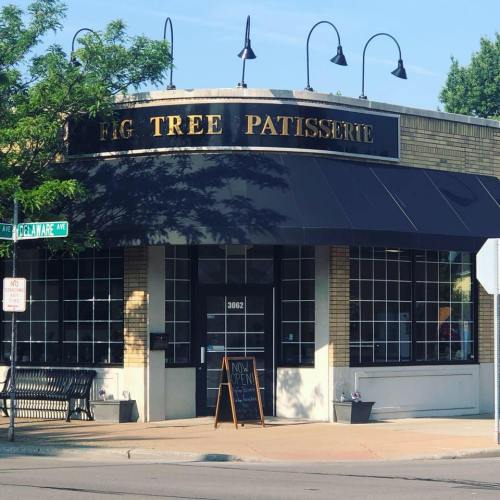 Exterior of Fig Tree Patisserie with a black awning, large windows, and a sign reading "Now Open."