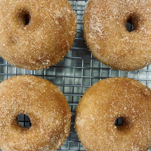 Four freshly baked donuts coated in sugar, resting on a wire cooling rack.