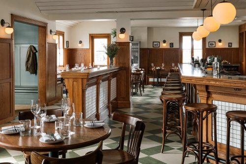 A stylish restaurant interior featuring wooden accents, round pendant lights, and a mix of tables and bar seating.
