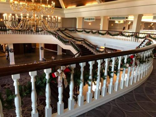 Elegant staircase adorned with festive garlands and decorations, under a grand chandelier in a hotel lobby.