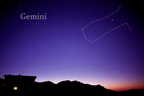 A twilight sky with the Gemini constellation outlined, above a silhouette of mountains and a house.