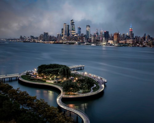 A scenic view of a city skyline at dusk, featuring a winding walkway and a lush island in the foreground.