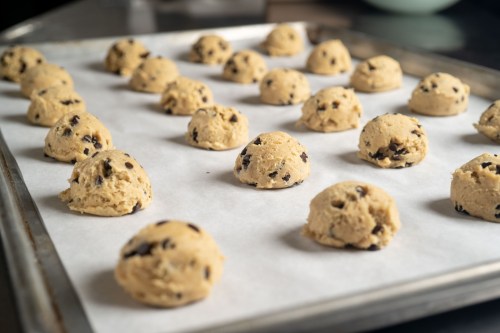 Cookie dough balls with chocolate chips arranged on a baking sheet lined with parchment paper.