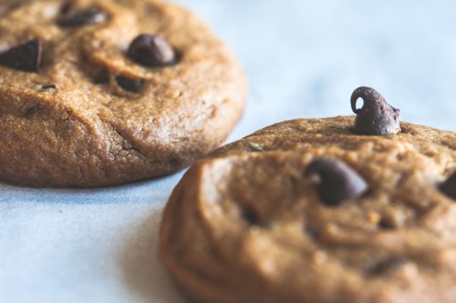 Close-up of two freshly baked chocolate chip cookies on parchment paper.