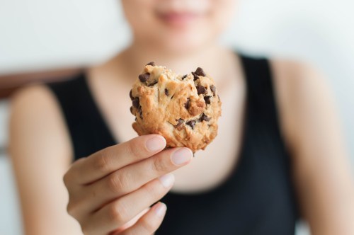 A person holds a half-eaten chocolate chip cookie, with a blurred background.
