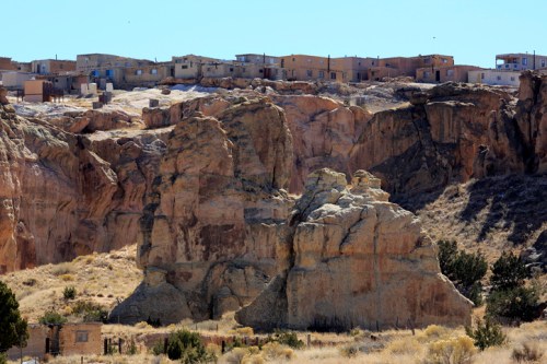 A rocky landscape with large formations in the foreground and a small village on a hill in the background.